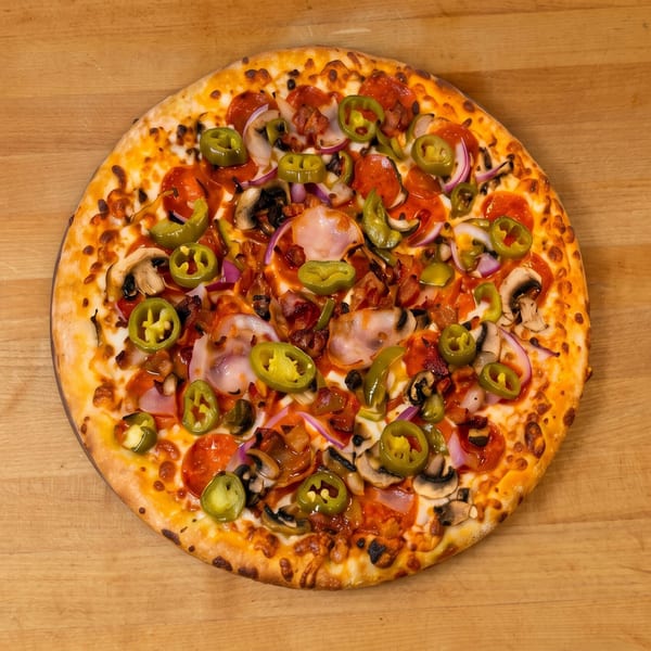 A whole pizza with pepperoni, bacon, mushrooms, red onions, and jalapeños on a wooden surface.