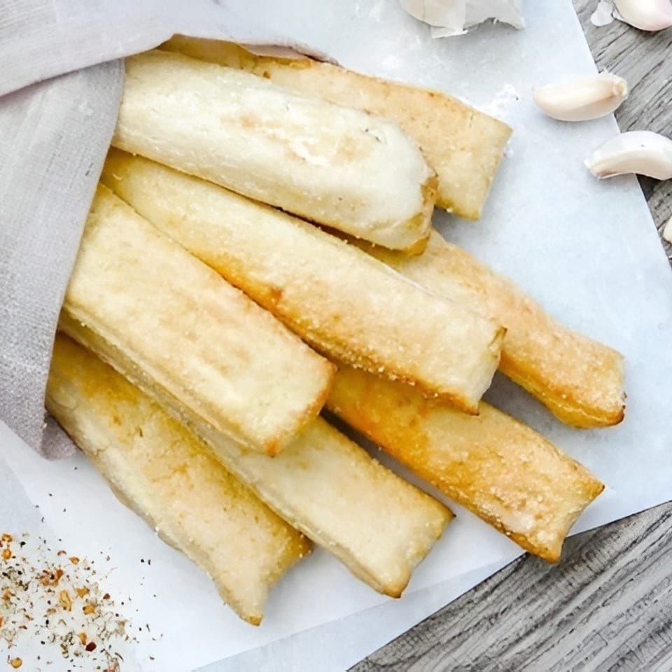 Golden-brown breadsticks wrapped in linen, with a side of red marinara sauce, basil, and garlic cloves.