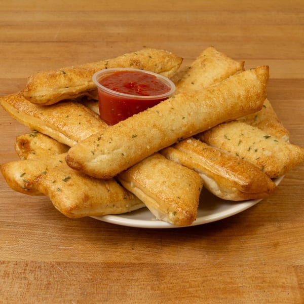 A plate of golden-brown breadsticks, some triangular, with a side of red marinara sauce.