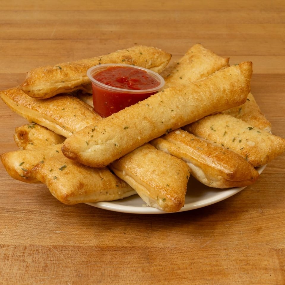 A plate of golden-brown breadsticks, some triangular, with a side of red marinara sauce.