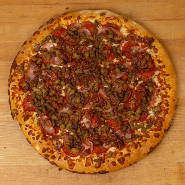 A whole meat lover's pizza with pepperoni, ham, and sausage on a wooden surface.