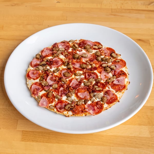 A small, round meat lover's pizza with pepperoni, sausage, and ham on a white plate.