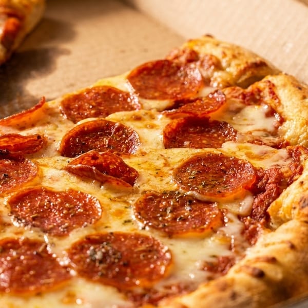 Close-up of a pepperoni pizza with melted cheese and a golden crust in a cardboard box.