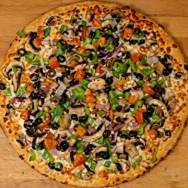 A whole vegetarian pizza with mushrooms, olives, bell peppers, onions, and tomatoes on a wooden surface.
