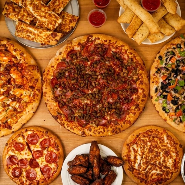 Overhead view of a wooden table laden with various pizzas, sides, and desserts.